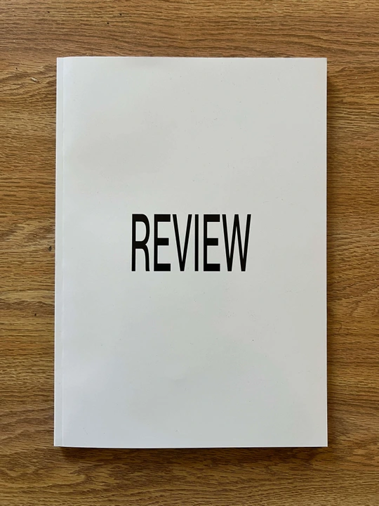 White REVIEW magazine on a wood surface